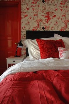 a bed with red and white pillows in a bedroom next to a wallpapered wall