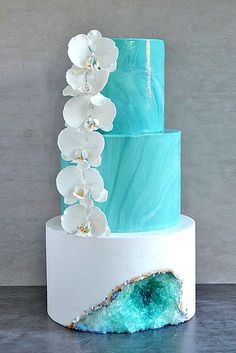 a three tiered cake with white orchids and blue marbled icing on top