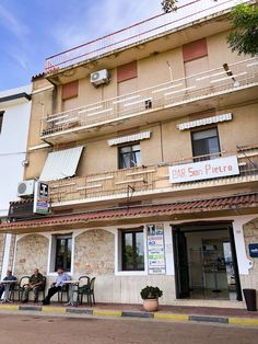 two people sitting at an outside table in front of a building with balconies