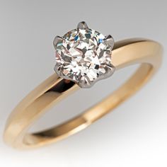 a yellow gold engagement ring with a round brilliant diamond in the center, on a white background