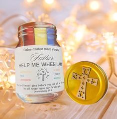 a glass jar with a cross on it next to a gold colored bible verse tag