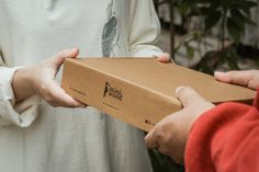 two people exchanging a box from another person's hand in front of some plants