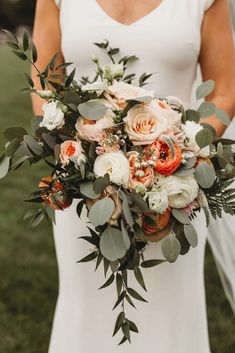 a bride holding a bouquet of flowers and greenery in her hand while standing on the grass