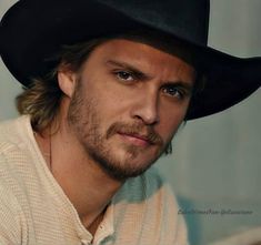 a close up of a person wearing a black cowboy hat and looking at the camera