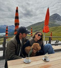 a man and woman sitting at a table with a dog in front of them on a cloudy day