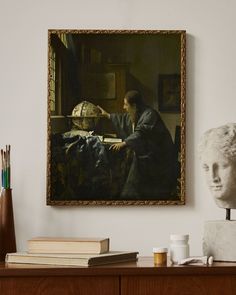 a painting hanging on the wall next to a table with books and other items in front of it