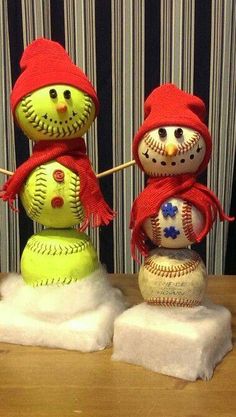 three snowmen with hats and scarves on top of each other, one is holding a baseball