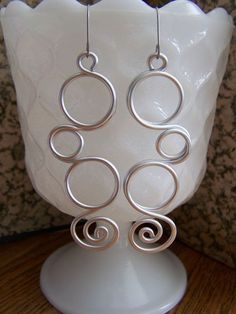 a pair of silver spiral earrings sitting on top of a white vase next to a wall