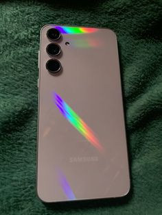 the back of a silver samsung phone on a green blanket with rainbow light coming from it