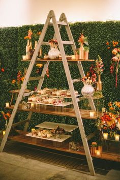 a wooden ladder is used as a display for cakes and desserts in front of a green wall