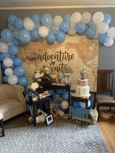 a table topped with cake and balloons next to a wall covered in blue and white balloons