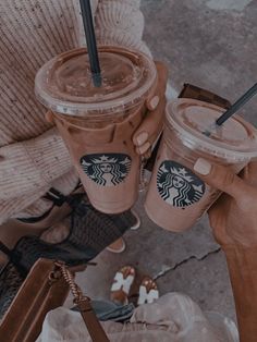 two people holding starbucks cups with straws in their hands and one is holding a cell phone