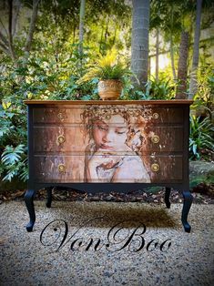 an old dresser with a painting on the top and bottom drawer is sitting in front of some trees