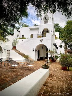 an outdoor patio with chairs and tables next to a white stucco building surrounded by trees