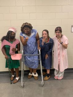 four women standing next to each other in front of a brick wall with a walker