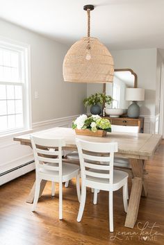 a dining room table with white chairs and a basket hanging from the ceiling