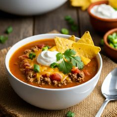 a white bowl filled with chili, cheese and tortilla chips on top of a wooden table