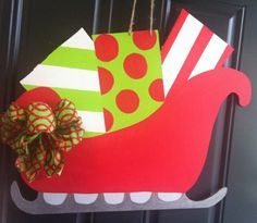 a christmas sleigh door hanger decorated with green and red paper, bows and polka dots