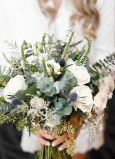 a woman holding a bouquet of white flowers and greenery in her hands, close up