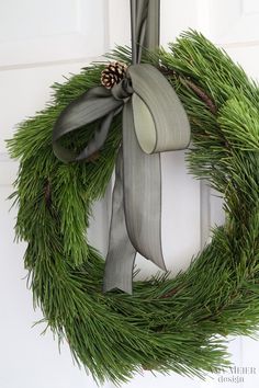 a christmas wreath hanging on the front door with a bow and pineconi in it