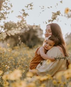 a woman holding a child in her arms while standing in a field full of yellow flowers