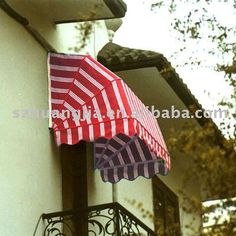 red and white striped umbrella hanging from the side of a building in front of trees