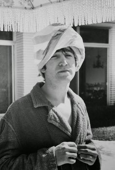 a woman with a towel on her head standing in front of a house wearing a hat