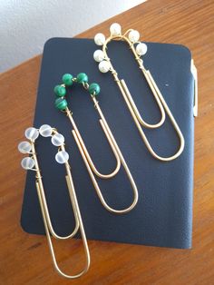 three pairs of earrings sitting on top of a black book next to a pair of green and white beads