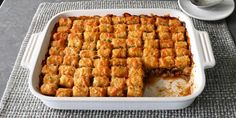 a casserole dish filled with tater tots next to a cup of coffee