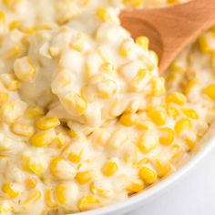 a wooden spoon scooping corn into a bowl with white cheese and sauce on top