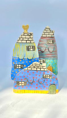 three colorful ceramic houses with faces painted on the front and back, sitting in the snow