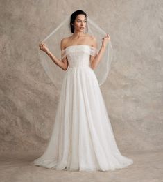 a woman in a white wedding dress with a veil on her head and hands behind her back