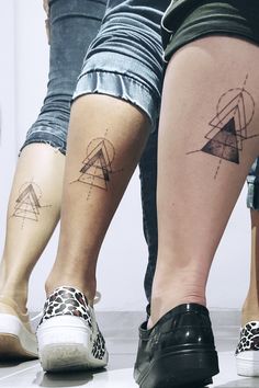 two people standing next to each other with matching tattoos on their legs, both showing geometric shapes