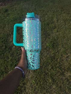 a person holding a blue and green coffee cup in their left hand on the grass