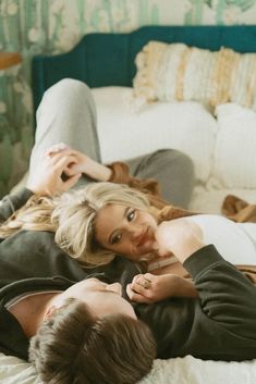 two people laying on a bed with one person touching the other's head and looking at the camera