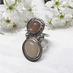 Not only does this ring have a dreamy peach moonstone but it also has an amazing cream moonstone too.  The coloring draws you.  Once you’re there, the pearlescent glow will keep you there.  The peach moonstone is a soft but rich terracotta color.  Equally important is the creamy coloring of the ivory moonstone.  Both stones sit nestled within silver bezel cups.  The peach stone is accented with a hammered silver braid.  A simple wire frame wraps around the ivory stone. Adjustable Oval Cabochon Moonstone Ring, Bohemian Oval Cabochon Moonstone Ring, Moonstone Rings With Natural Stones, Moonstone Oval Cabochon Ring, Unique Handmade Oval Cabochon Moonstone Ring, Handmade Unique Oval Moonstone Ring, Round Cabochon Moonstone Ring, Unique Cabochon Moonstone Ring, Elegant Untreated Moonstone Ring