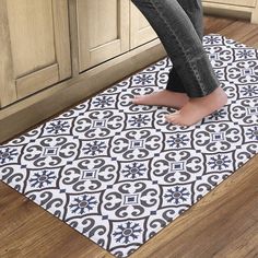 a person standing on the floor in front of a kitchen door mat with an ornate design