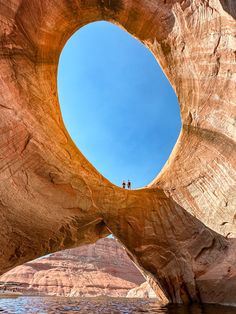 two people are standing on the edge of a large rock formation with water in front of them