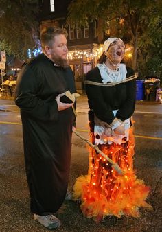 two people dressed in costumes standing next to each other on the street with lights all around them