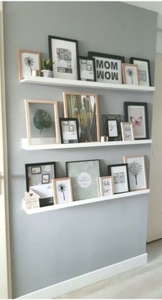 some white shelves with pictures on them and framed photos hanging up against the wall behind them