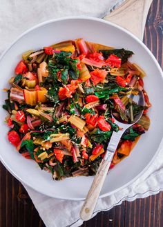 a white bowl filled with vegetables on top of a wooden table next to a spoon