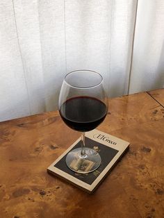 a glass of red wine sitting on top of a wooden table next to a book