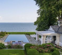 an outdoor swimming pool surrounded by lush green grass and flowers with the ocean in the background