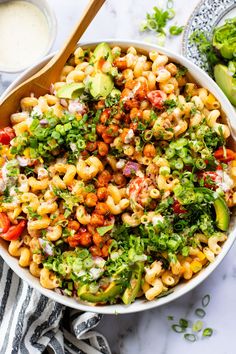 a bowl filled with pasta salad next to two bowls of ranch dressing and avocado