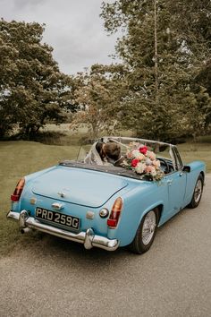 a bride and groom kissing in the back of an old blue convertible car on their wedding day