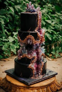 a three tiered black cake with crystals on top and greenery in the background