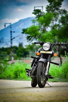 a black motorcycle parked on the side of a road next to some grass and trees