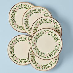 four plates with holly designs on them sitting next to each other in front of a blue background