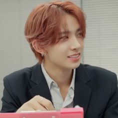 a person sitting at a table with a pink laptop in front of him and wearing a suit