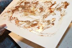 a person holding up a piece of paper with brown and white paint splattered on it